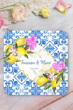 a blue and white tile with yellow lemons and pink flowers on it, next to some roses