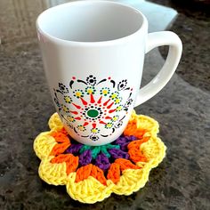 a white coffee cup sitting on top of a table next to a crocheted coaster