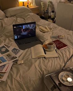 a laptop computer sitting on top of a bed next to an open book and cup