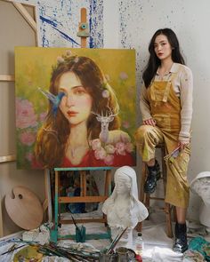 a woman standing in front of an easel with paintings on the ground behind her