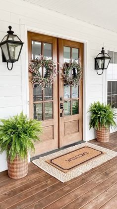 two potted plants sitting on the front porch next to a door with wreaths