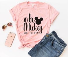 a pink shirt with the phrase oh mickey you so fine on it next to sunglasses and phone