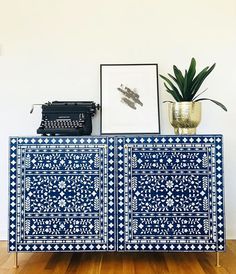 a blue and white painted cabinet with a typewriter on top next to a potted plant