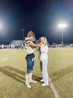 two people standing on a football field with one holding the other's arm over his shoulder