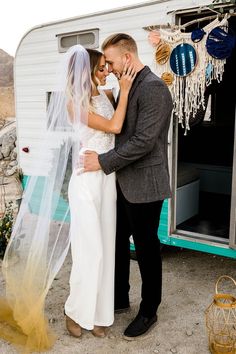 a bride and groom standing in front of a trailer with their wedding veil pulled back