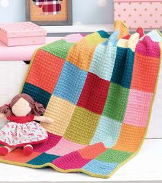 a crocheted blanket with a doll sitting on the floor in front of it