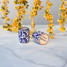 two blue and white cups sitting next to each other on a table with yellow flowers in the background