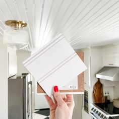 a person holding up some white tiles in a kitchen with an oven and stove top