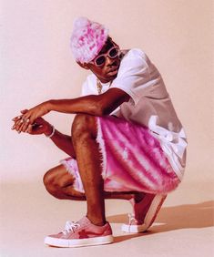 a man with pink hair and sunglasses sitting on a skateboard in front of a white background