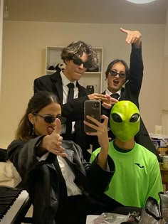 three people dressed in alien costumes taking pictures with their cell phones and pointing at them