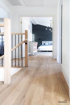 an empty hallway leading to a bedroom with a bed in the corner and wooden floors