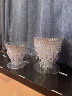 two glass vases sitting on top of a black shelf next to a window curtain