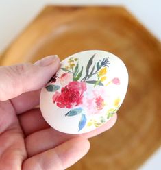 a hand holding an egg with flowers painted on it