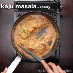 a person stirring food in a pan on top of a wooden table with the words kaju masala ready