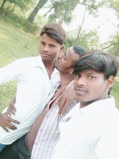 three men are posing for the camera in front of some trees and grass with their arms around each other