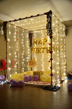 a birthday party setup with balloons, streamers and lights on the wall behind it