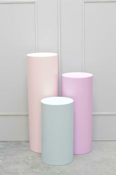 three pastel colored vases sitting next to each other on the floor in front of a white wall