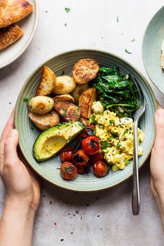 two hands holding a plate of food with eggs, potatoes and spinach on it