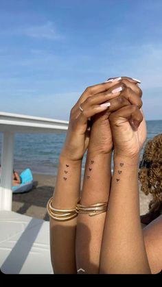 two women with matching tattoos on their arms holding each other's hands in front of the ocean