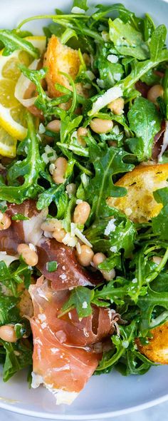 a white plate topped with salad and lots of meat on top of it's leaves