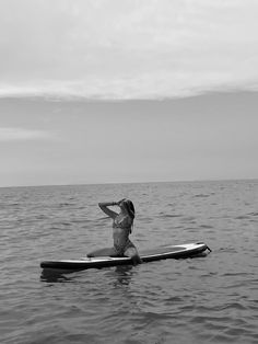 a woman sitting on top of a surfboard in the middle of the ocean with her arms behind her head