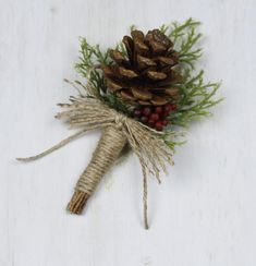 a pine cone tied to twine with berries and greenery next to it on a white surface