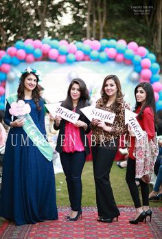 three women holding signs in front of an arch with balloons and streamers on it