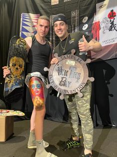 two men standing next to each other holding skateboards and giving the thumbs up sign