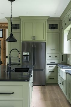 a kitchen with green cabinets and an island in front of the sink is lit by a pendant light