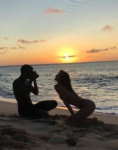 a man and woman sitting on the beach at sunset