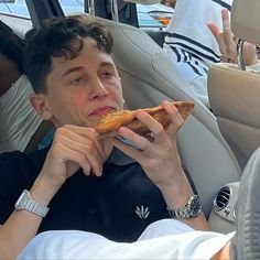 a man sitting in the back seat of a car eating a piece of pizza with his hands