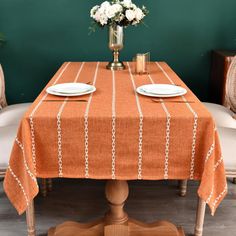 an orange tablecloth with white plates and flowers on it in front of a green wall