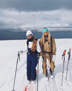 two women standing on top of a snow covered slope wearing skis and holding ski poles