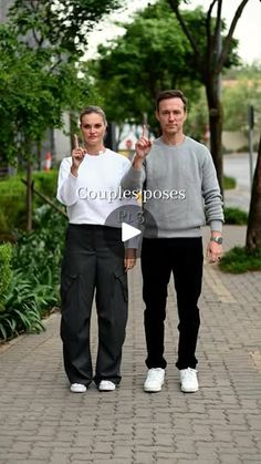 a man and woman standing next to each other on a brick walkway with trees in the background