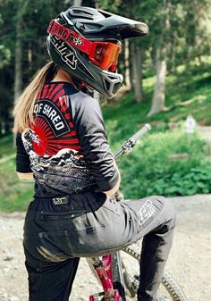 a woman sitting on top of a bike wearing a helmet and riding it down a dirt road