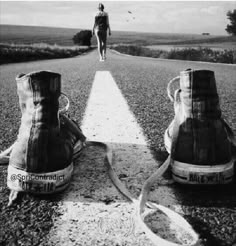 two pairs of shoes sitting on the side of an empty road with a person walking behind them