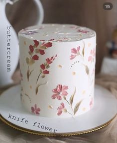 a white cake with pink flowers on it sitting on a plate next to a teapot