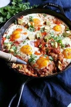 two eggs are in a skillet with avocado and tomato toppings on top