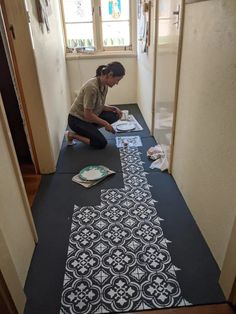 a woman kneeling down on the floor to paint a decorative design in front of a window