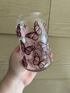 a hand holding a glass with pink butterflies on it