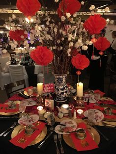 the table is set with red and white plates, silverware, candles and flowers