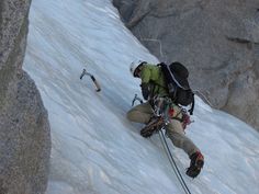 a man climbing up the side of a snow covered mountain with skis and poles