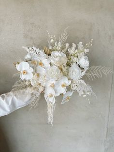 a bridal bouquet with white flowers and greenery on the side of a wall