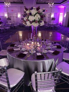 a table set up for a formal dinner with purple lighting and flowers in the center