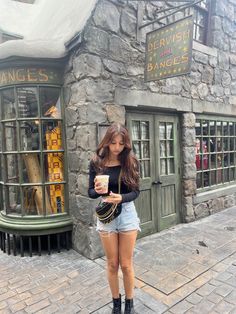 a woman standing in front of a stone building holding a cup and looking at her cell phone