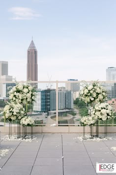 an outdoor ceremony setup with white flowers and greenery in front of a cityscape