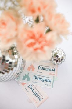 there is a mirror ball and some flowers on the table next to tickets for disneyland