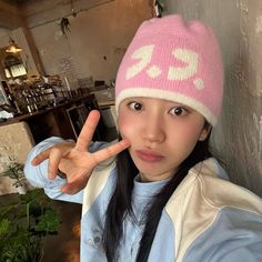 a young woman wearing a pink hat making the peace sign