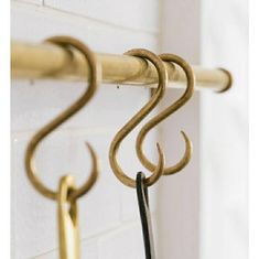 two metal hooks hanging on a white brick wall next to a black and gold towel rack