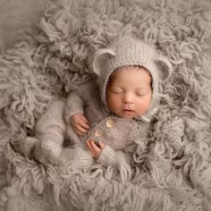 a baby in a knitted bear outfit sleeping on a fluffy blanket with its eyes closed